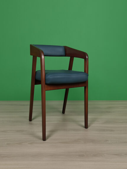 A stylish wooden armchair (Model: DDC 1409) with a curved frame made of Akashi/Mahogany, upholstered in black leather, placed on a light wooden floor with a green background.