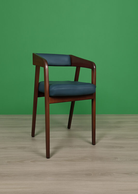 A stylish wooden armchair (Model: DDC 1409) with a curved frame made of Akashi/Mahogany, upholstered in black leather, placed on a light wooden floor with a green background.